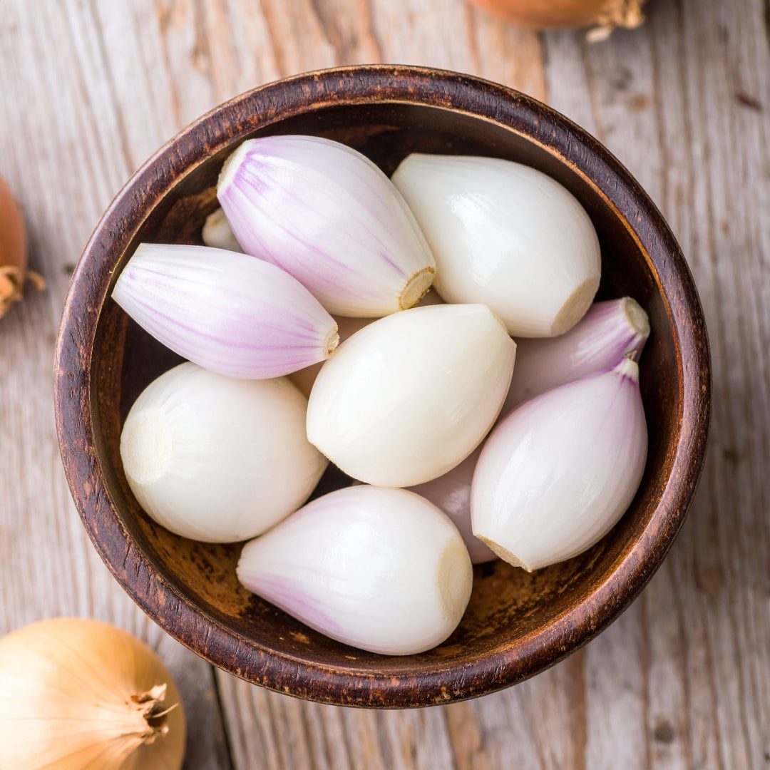 Peeled shallots in a brown bowl on a wooden table